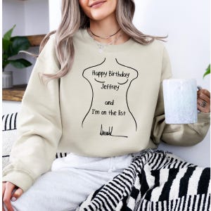 K&ouml;nnte beinhalten: Beiges Sweatshirt mit schwarzer Umrisszeichnung eines Torsos und dem Text "Happy Birthday Jeffrey and I'm on the list". Das Sweatshirt ist aus weichem Material.