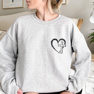May include: Gray sweatshirt with a black heart and cross graphic.