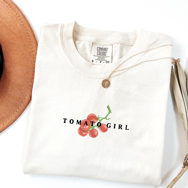 May include: A white t-shirt with the text "TOMATO GIRL" and a small illustration of red tomatoes on a vine.