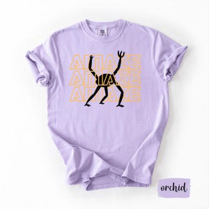 May include: A light purple t-shirt with the word "AMAZE" repeated three times in a yellow-orange color. A black graphic of a stick figure is in the center. The shirt is a soft, comfortable material.