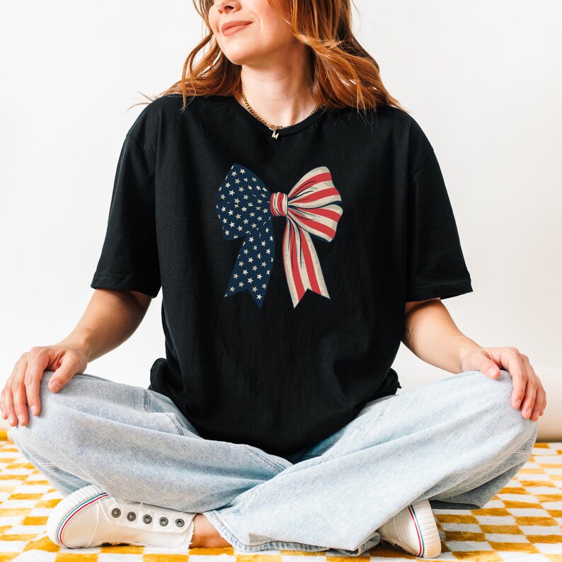Peut inclure: Un t-shirt noir avec un n&oelig;ud rouge, blanc et bleu imprim&eacute; sur le devant. Le n&oelig;ud est compos&eacute; du drapeau am&eacute;ricain.