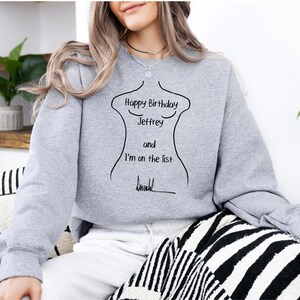 K&ouml;nnte beinhalten: Ein hellgraues Sweatshirt mit einer schwarzen Umrisszeichnung eines Torsos und dem Text "Happy Birthday Jeffrey and I'm on the list" in Schwarz. Das Sweatshirt hat einen l&auml;ssigen Stil.