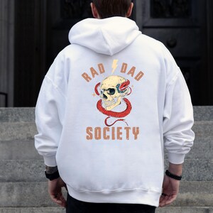 May include: White hoodie with a graphic print of a skull with a snake wrapped around it. The text "Rad Dad Society" is printed below the skull.
