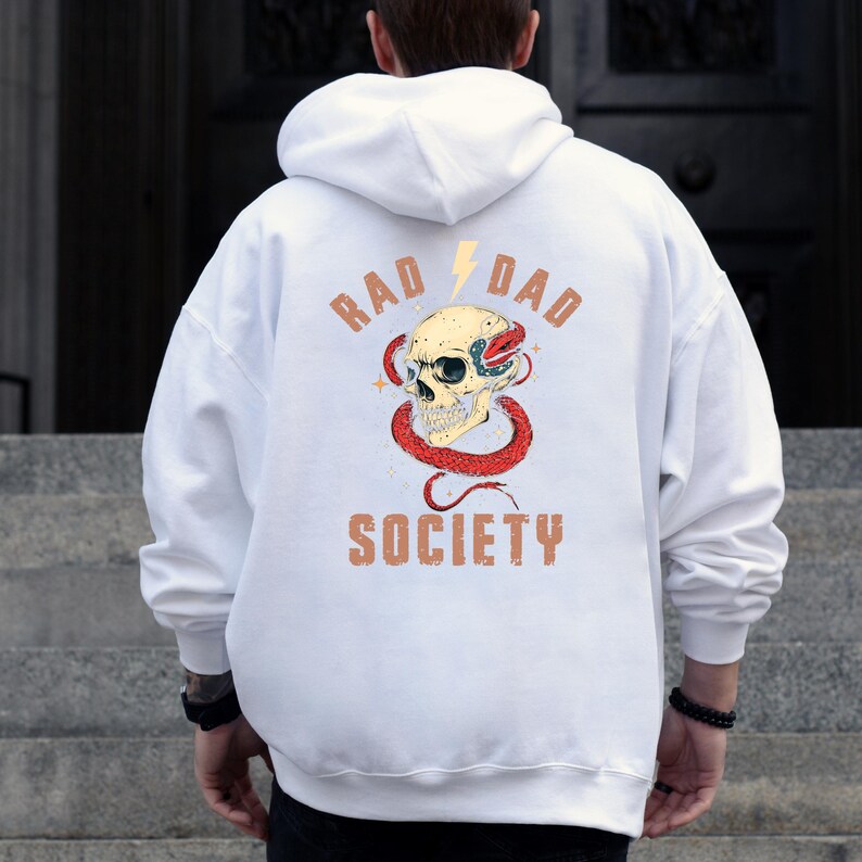 May include: White hoodie with a graphic print of a skull with a snake wrapped around it. The text "Rad Dad Society" is printed below the skull.