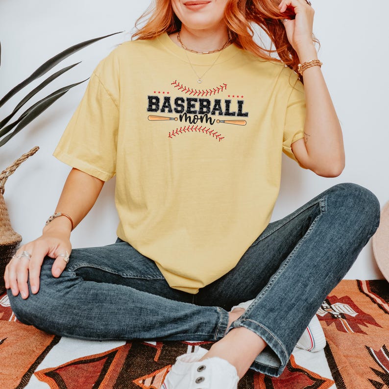 May include: A yellow t-shirt with the text "Baseball Mom" in black with a red baseball stitch design and two baseball bats.