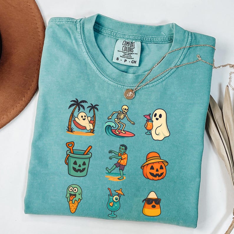 May include: Teal Comfort Colors t-shirt with a variety of Halloween-themed graphics. The graphics include a ghost in a hammock, a skeleton surfing, a ghost with a cocktail, a jack-o'-lantern bucket, a zombie, a pumpkin with a hat, ice cream, a cocktail, and candy corn.