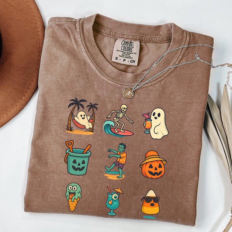 May include: Brown Comfort Colors t-shirt featuring a collection of Halloween-themed illustrations. The graphics include a ghost in a hammock, a skeleton surfing, a ghost with a cocktail, a jack-o'-lantern bucket, a zombie, and a candy corn with sunglasses.