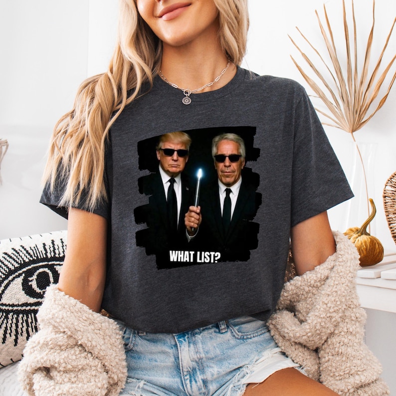 K&ouml;nnte beinhalten: Dunkelgraues T-Shirt mit einer Grafik von zwei M&auml;nnern in schwarzen Anz&uuml;gen und Sonnenbrillen, die einen leuchtenden Zauberstab halten. Der Text "WHAT LIST?" ist darunter gedruckt. Das T-Shirt ist l&auml;ssig.