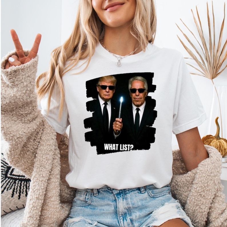 K&ouml;nnte beinhalten: Wei&szlig;es T-Shirt mit einer Grafik von zwei M&auml;nnern in schwarzen Anz&uuml;gen und Sonnenbrillen, einer h&auml;lt einen leuchtenden Zauberstab. Der Text "WHAT LIST?" befindet sich unter dem Bild. Das Shirt ist ein l&auml;ssiger Stil.