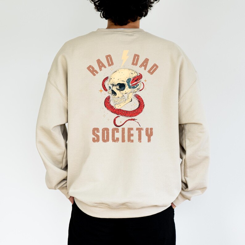 May include: A beige sweatshirt with a graphic print of a skull with a snake wrapped around it. The text "Rad Dad Society" is printed below the skull.