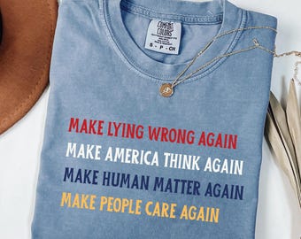 Può includere: Una maglietta blu con il testo "Make Lying Wrong Again", "Make America Think Again", "Make Human Matter Again" e "Make People Care Again" stampato in rosso, bianco, blu e giallo.