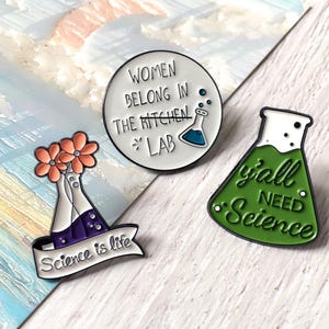 Peut inclure: Trois épingles en émail avec des motifs sur le thème de la science. Une épingle est un cercle blanc avec le texte "WOMEN BELONG IN THE LAB". Une autre épingle est un flacon vert avec le texte "y'all NEED Science". La troisième épingle a un flacon avec des fleurs et le texte "Science is life".