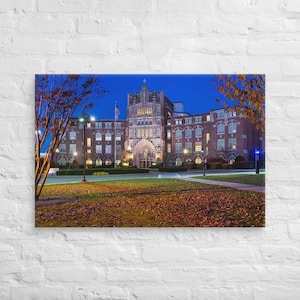 May include: A brick building with a large arched entrance and many windows. The building is lit up at night and there are trees and a grassy lawn in front of it.