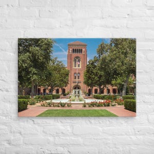 May include: A red brick building with a clock tower and a fountain in front of it. The building is surrounded by green trees and a grassy lawn.