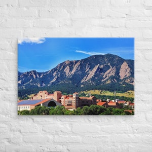May include: A panoramic view of a university campus with red brick buildings and a large mountain range in the background. The sky is blue with white clouds.