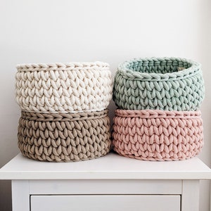 Peut inclure: Quatre paniers de rangement ronds fabriqués en cordon tricoté épais et volumineux. Les paniers sont disposés en deux piles, dans des tons crème, vert sauge, beige et rose pâle. Chaque panier présente un motif de maille tressée texturé.