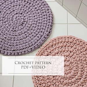 Könnte beinhalten: Zwei gehäkelte runde Teppiche in einem Badezimmer. Der Teppich links ist helllila und der Teppich rechts ist hellrosa. Der Text "CROCHET PATTERN PDF+VIDEO" wird in der Mitte des Bildes angezeigt.
