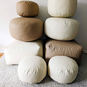 Peut inclure: Un ensemble de six poufs ronds et rectangulaires de couleur beige et crème. Les poufs sont disposés en deux piles de trois, les poufs ronds étant en haut.