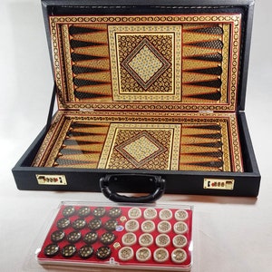Könnte beinhalten: Ein schwarzes Holzspielbrett mit aufwendigen Intarsien in Braun-, Rot- und Goldtönen. Das Brett ist geöffnet und zeigt ein Backgammon-Spielbrett und ein Schachbrett. Das Brett befindet sich in einem schwarzen Transportkoffer mit Griff. Vor dem Brett befindet sich ein durchsichtiger Plastikkoffer mit schwarzen und weißen Spielsteinen.