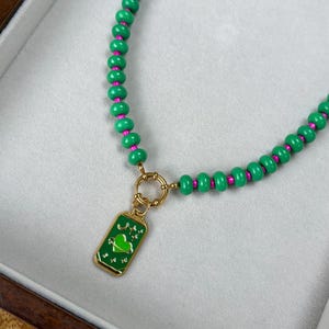 May include: A green beaded necklace with pink accents and a gold clasp. The necklace features a rectangular pendant with a green heart design and gold trim. The pendant has the text "yo yo yo".