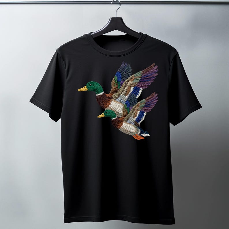 A black t-shirt with a colorful embroidered image of two ducks in flight.