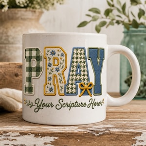 Könnte beinhalten: Ein weißer Keramikbecher mit dem Wort PRAY in großen, dekorativen Buchstaben. Das P ist grün kariert, das R hat ein blaues Blumenmuster, das A ist grün-weißes Hahnentrittmuster mit einer gelben Schleife und das Y ist einfarbig blau. Darunter steht Your Scripture Here.