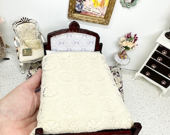May include: Miniature bedroom set with a dark wood bed frame and a cream-colored, patterned blanket. The headboard has a light blue and white patterned fabric. The scene includes a white chair, a small table with flowers, and framed pictures on the wall.