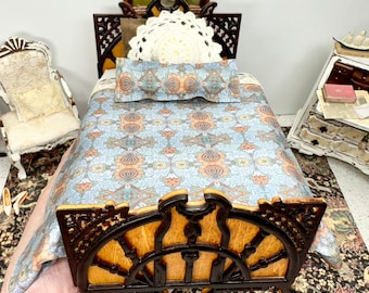 May include: Miniature wooden bed with a detailed headboard and footboard. The bed is adorned with a floral patterned comforter and pillow. A framed painting hangs above the bed, and a small chair and dresser are visible in the background. The bed is held by a hand.