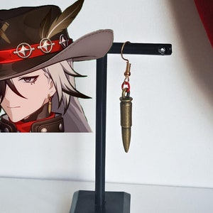 Peut inclure: Une paire de boucles d'oreilles en forme de balle dorées sur un support noir. Les boucles d'oreilles sont suspendues à un crochet doré.