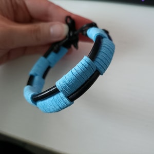 May include: A blue and black bracelet with a braided design. The bracelet is made of leather and fabric.