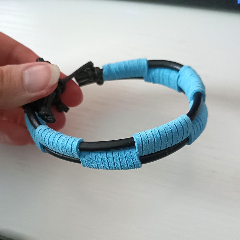 May include: A blue and black braided bracelet with a simple design. The bracelet is made of leather and has a woven pattern.