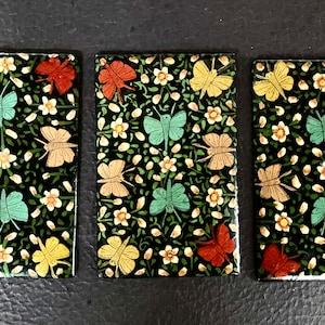 May include: Three rectangular tiles with a black background and a repeating pattern of colorful butterflies and white flowers.