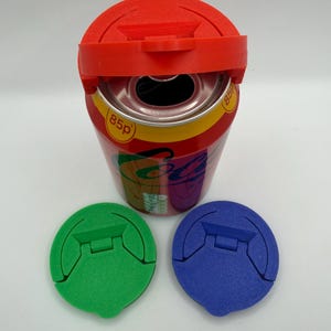May include: A red plastic lid sits atop a soda can, with two additional green and blue lids. The can has a colourful label with the text "85p". The lids appear to be designed to fit the can.