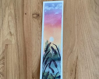 May include: Watercolor bookmark featuring a sunset scene with a gradient of pink, orange, and blue hues. Silhouetted wheat stalks and a sun are in the foreground. The bookmark is rectangular with a white border.