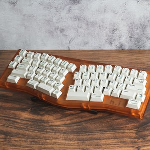 Pode incluir: Um teclado de design personalizado, de cor laranja, com teclas brancas e letras cirílicas. O teclado está sobre uma superfície de madeira.