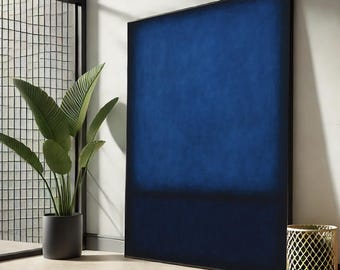 May include: A large, rectangular abstract painting with a deep blue gradient, transitioning to a darker shade at the bottom. The artwork is framed in black and leans against a white wall. A potted plant and a decorative gold metal basket are in the foreground.