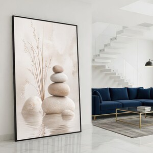 May include: Framed art print depicting a stack of smooth, beige stones, with a sprig of dried grass, reflected in water. The artwork has a neutral colour palette and a minimalist aesthetic, suitable for home decor.