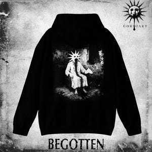 May include: Black hoodie featuring a grayscale graphic of a figure with a star-shaped mask seated in a dark room. The word "BEGOTTEN" is printed at the bottom. The hoodie also has the "GORDiART" logo with a sun design.