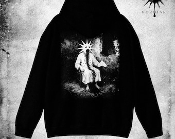 May include: Black hoodie featuring a grayscale graphic of a figure with a star-shaped mask seated in a dark room. The word "BEGOTTEN" is printed at the bottom. The hoodie also has the "GORDiART" logo with a sun design.