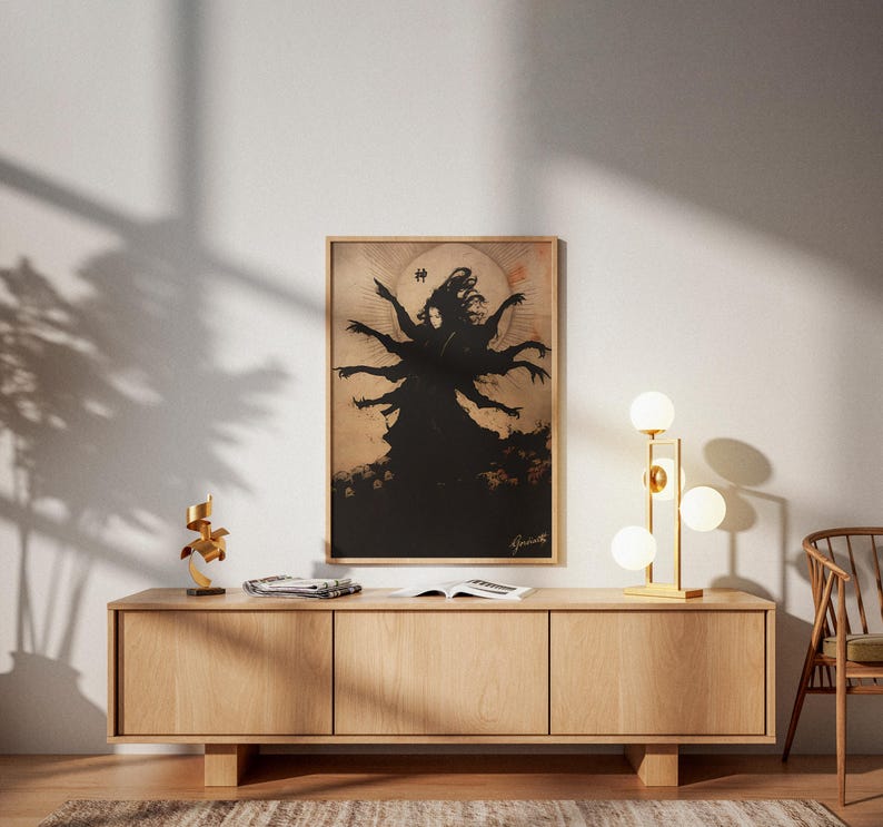 May include: A framed artwork featuring a black silhouette of a multi-armed figure against a tan background. The artwork is displayed above a light wood cabinet with a gold lamp and decorative sculpture.