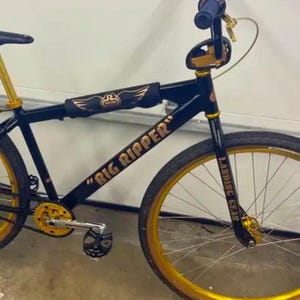 May include: Black and gold bicycle with "Big Ripper" and "Landing Gear" written on the frame. The bicycle has a black seat and gold handlebars.