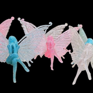 Op de afbeelding: Vijf iriserende fee-figuurtjes met glittervleugels. De feeën staan in verschillende poses en hebben verschillende gekleurde vleugels, waaronder roze, blauw en wit.