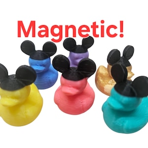May include: A collection of colorful duck-shaped magnets, each with black mouse ears. The ducks are in various colors, including yellow, blue, pink, purple, gold, and teal. The word "Magnetic!" is written in red above the ducks.