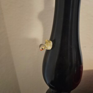 May include: A small, gold and white glittery bird figurine is attached to a black lamp base.