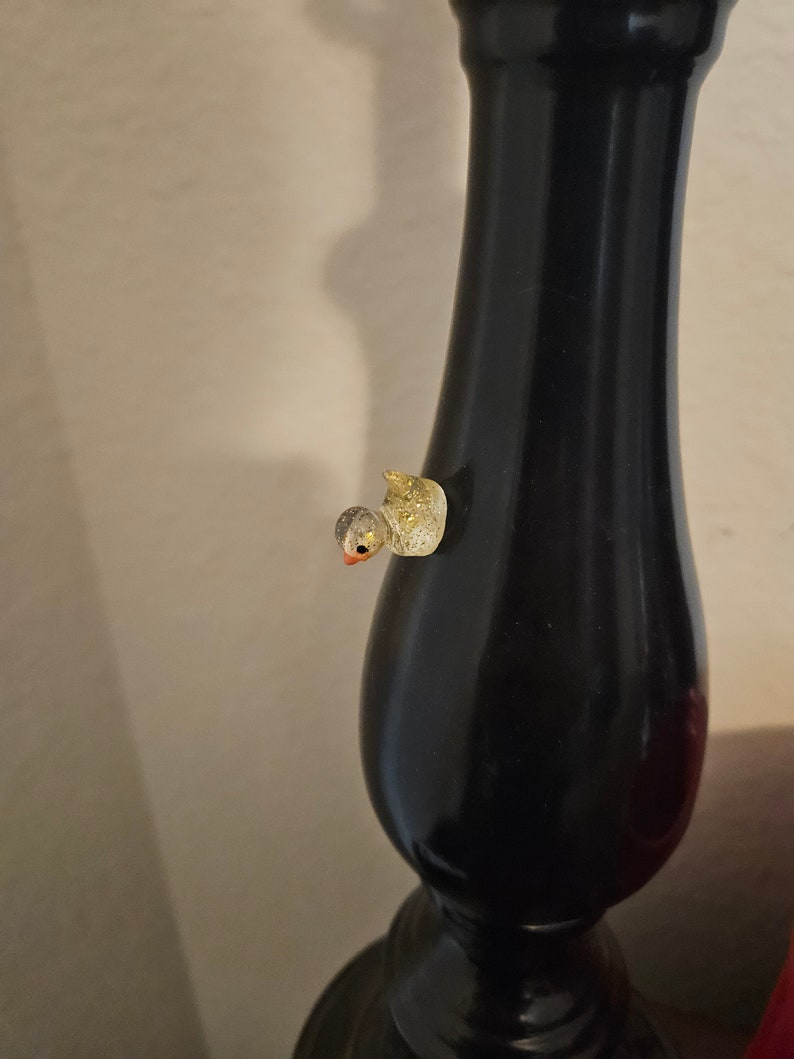 May include: A small, gold and white glittery bird figurine is attached to a black lamp base.