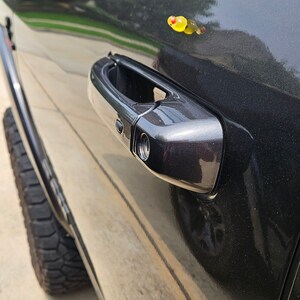 May include: A black truck door with a chrome door handle and a small yellow object on the door.