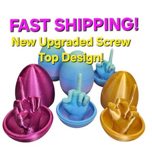 Puede incluir: Tres huevos impresos en 3D, cada uno de un color diferente: rosa, azul y dorado. Cada huevo tiene una tapa de rosca que revela un gesto de dedo medio en el interior. El texto "¡ENVÍO RÁPIDO! ¡Nuevo diseño de tapa de rosca mejorado!" se muestra sobre los huevos.