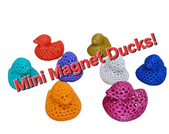 May include: A set of eight mini magnet ducks in various colors, including red, orange, yellow, blue, green, white, and pink. The ducks are made of a 3D printed material with a lattice design. The text "Mini Magnet Ducks!" is written in red letters across the image.
