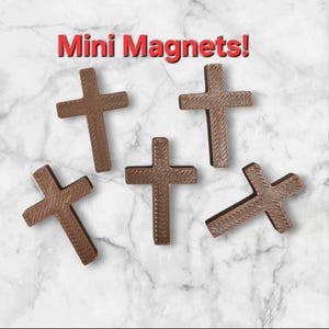 May include: Five brown cross-shaped magnets are displayed against a marble background. The text "Mini Magnets!" is in red at the top. The crosses have a textured surface.