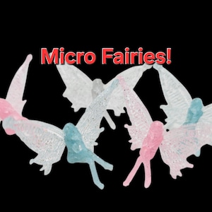 May include: Several small fairy figurines with translucent wings and bodies in shades of pink and blue are arranged against a black background. The text "Micro Fairies!" is displayed in red above the figurines.